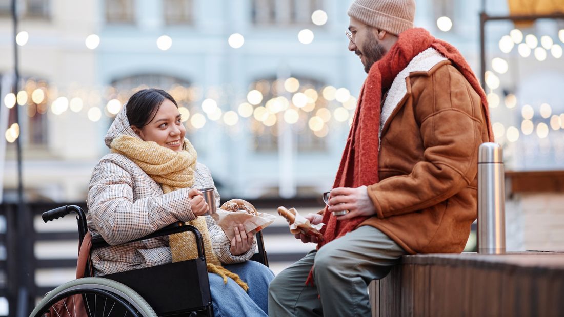 A couple talking over hot drinks at an outdoor market in the evening
